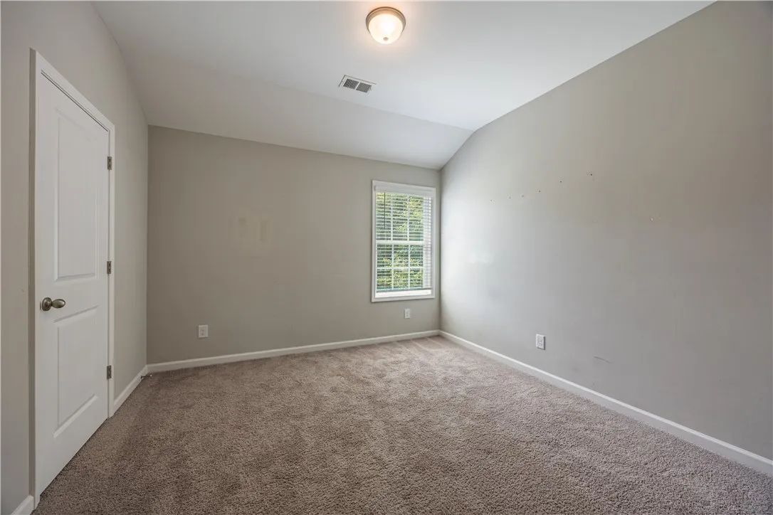 A well-lit bedroom features plush carpeting and a bright window with outdoor views.