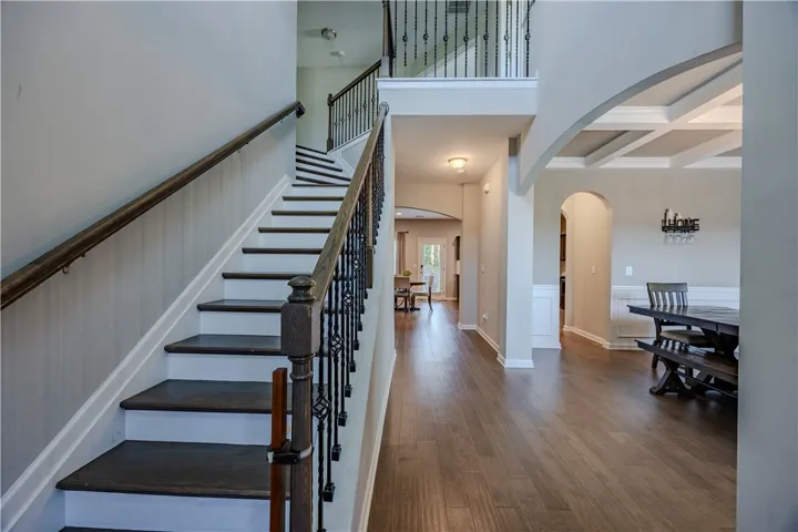 A grand two-story staircase with wrought iron balusters complements rich hardwood flooring and a coffered ceiling in this welcoming foyer.