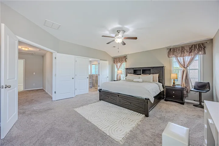 A spacious primary bedroom featuring plush carpeting, a vaulted ceiling, and ample natural light from large windows.
