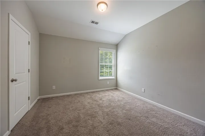 A well-lit bedroom features plush carpeting and a bright window with outdoor views.