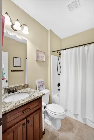 Located next to the guest bedroom,  this guest bath with granite counters  and a warm wood vanity elevate this inviting bathroom.