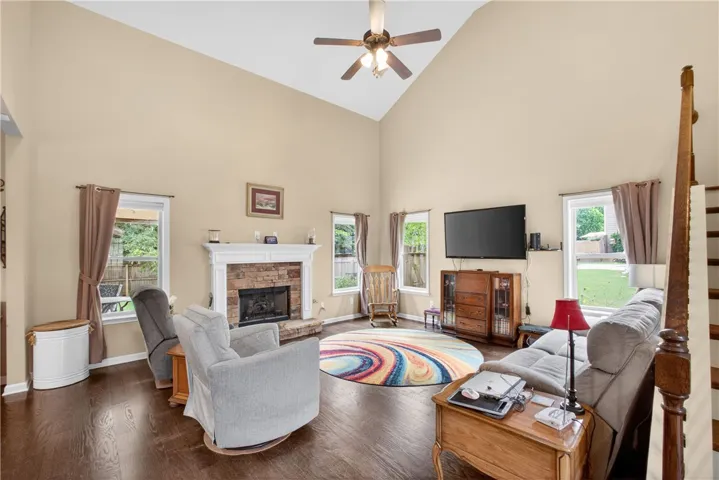 A spacious living room features soaring vaulted ceilings, rich hardwood flooring, and a stone fireplace with a classic mantel.