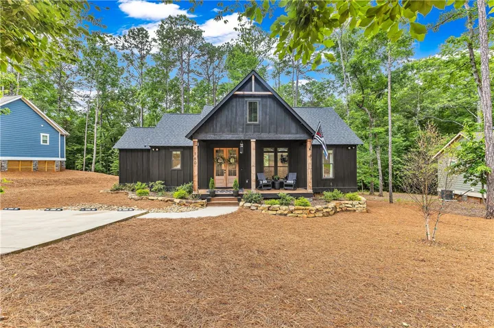 A charming modern farmhouse exterior features a welcoming porch, dark siding, and a well-maintained, natural landscape.