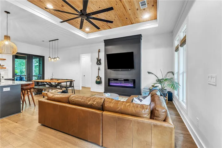 A striking modern fireplace and television display anchor this open-concept living space, featuring warm wood floors and abundant natural light.