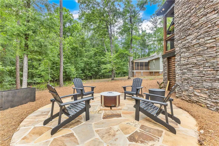 An inviting stone patio with fire pit offers a natural gathering space amidst towering trees.