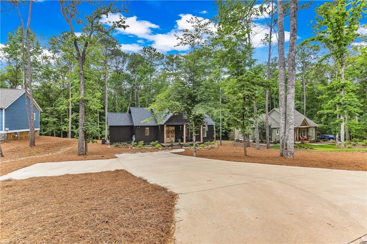 A dark-toned cottage is nestled among mature trees with a sweeping concrete driveway leading to its inviting entrance.