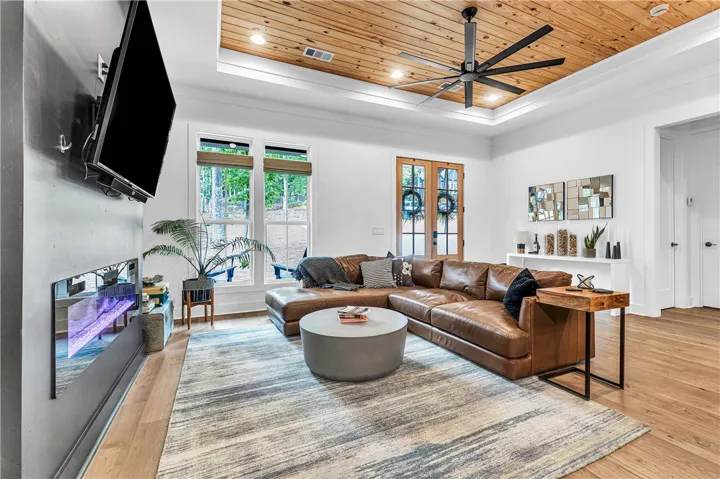 A warm, inviting living area featuring wood floors, recessed lighting, and a unique wood-paneled tray ceiling.