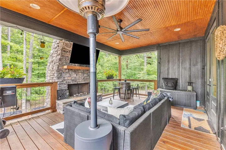An inviting outdoor living area features a robust stone fireplace and a wood plank ceiling, offering comfortable entertaining amidst lush trees.