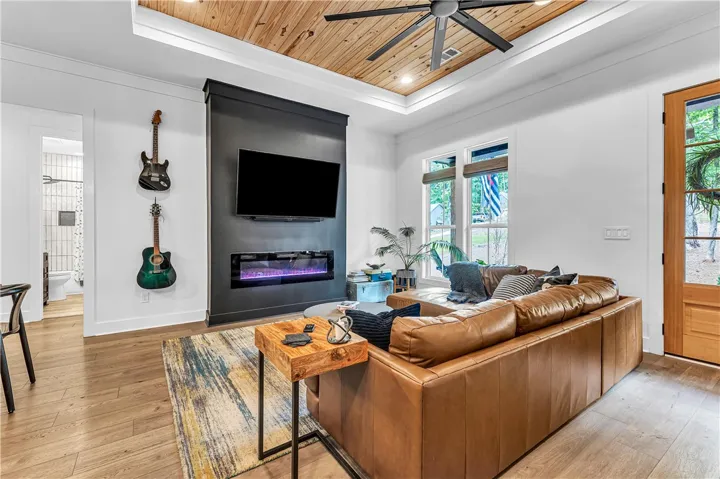 A striking black accent wall with a modern fireplace anchors this naturally illuminated living space, complemented by a unique wood plank ceiling.
