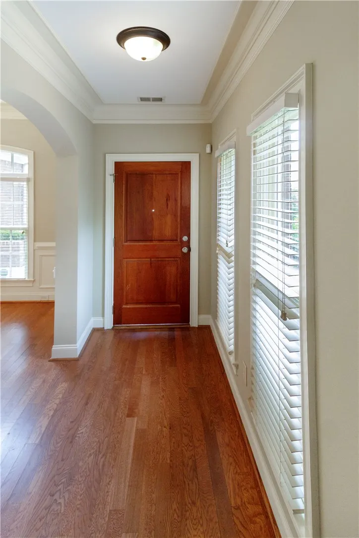 A warm wooden entry door welcomes you to a hallway featuring gleaming hardwood floors and natural light.
