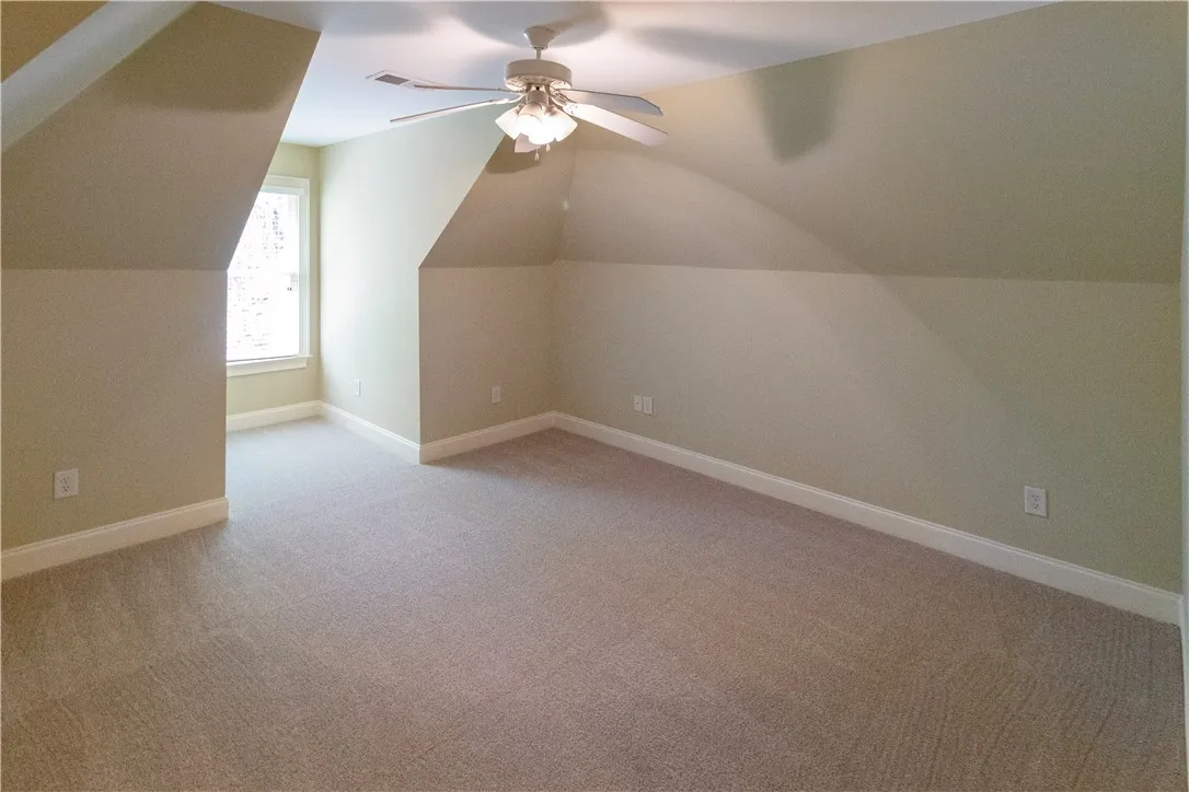 A well-lit, neutral-toned space ready for your personal touch, featuring soft carpeting and a ceiling fan.