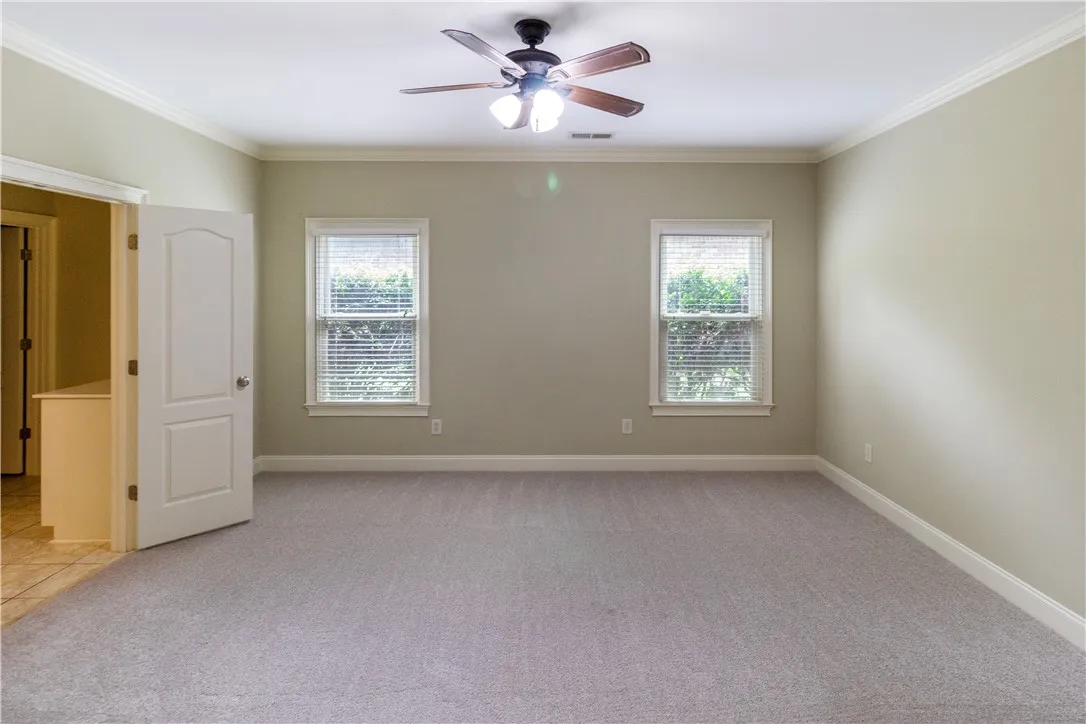 A well-proportioned primary bedroom with new gray carpeting, crown molding, and a refreshing ceiling fan.