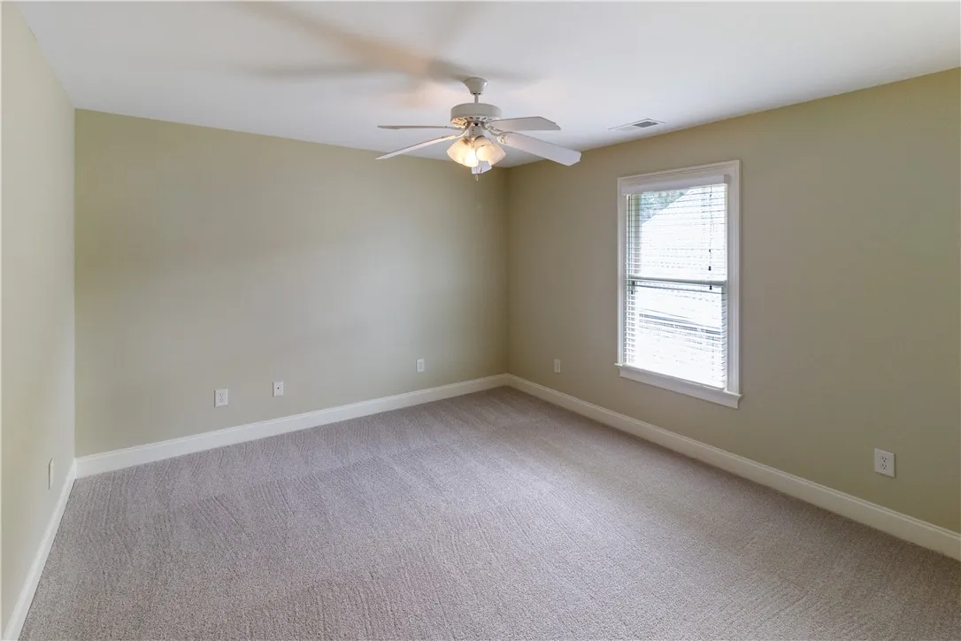 A well-lit bedroom offering a cozy retreat with soft carpet and a cooling ceiling fan.