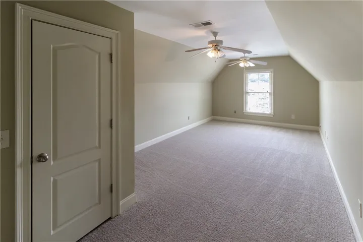 A well-lit bonus room features soft carpet and a vaulted ceiling with two ceiling fans.