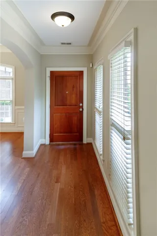 A warm wooden entry door welcomes you to a hallway featuring gleaming hardwood floors and natural light.