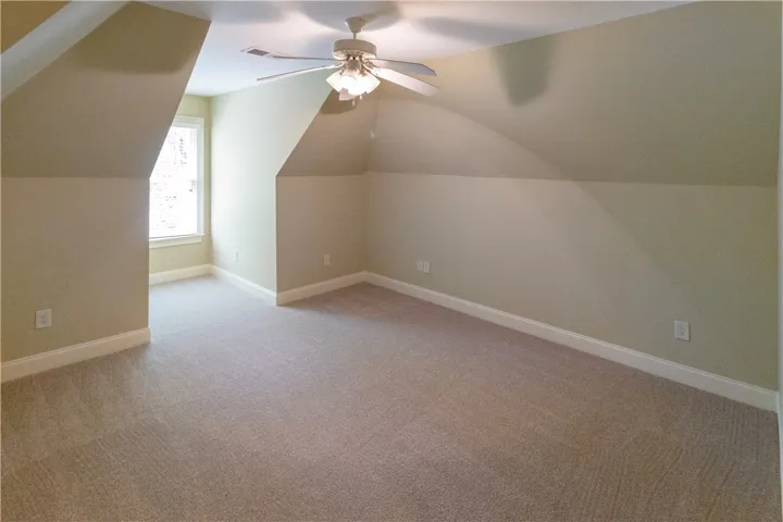 A well-lit, neutral-toned space ready for your personal touch, featuring soft carpeting and a ceiling fan.