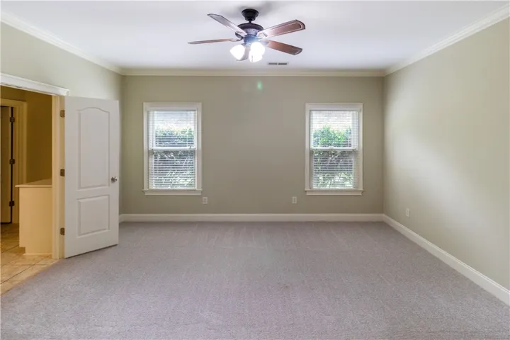 A well-proportioned primary bedroom with new gray carpeting, crown molding, and a refreshing ceiling fan.