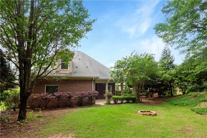 A verdant backyard with mature trees and a brick fire pit offers a serene outdoor retreat.