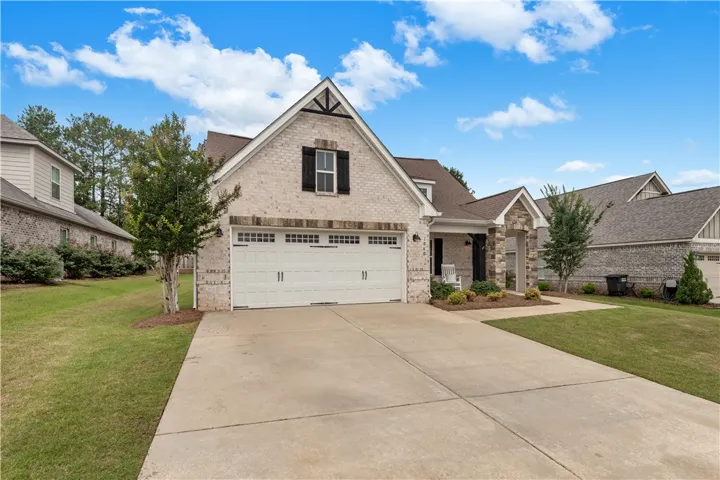 A cream-colored brick home with a gable roof and attached garage awaits, featuring dark shutters and a welcoming entry.
