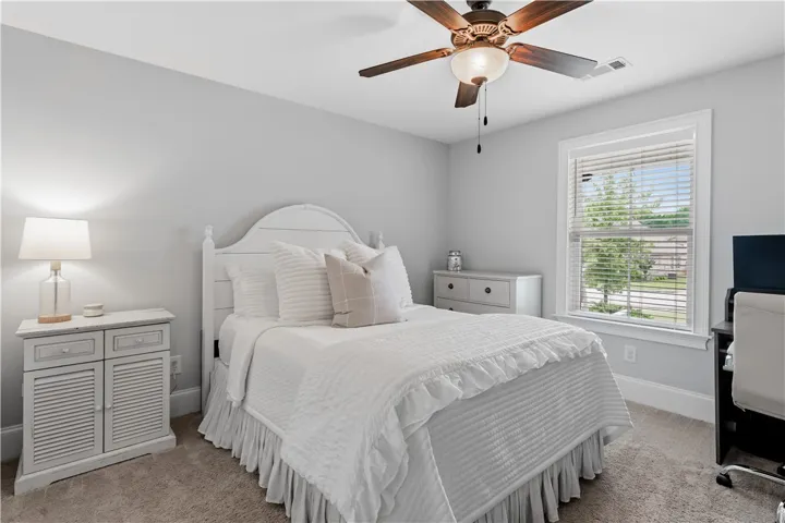 A well-lit room offers comfort, featuring a ceiling fan and soft carpeting for tranquil living.