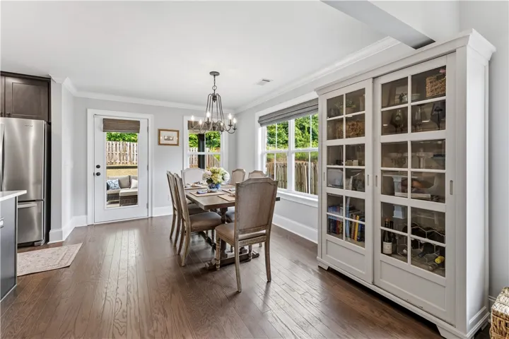 Hardwood flooring extends throughout this well-lit dining area, featuring a modern chandelier and outdoor views.