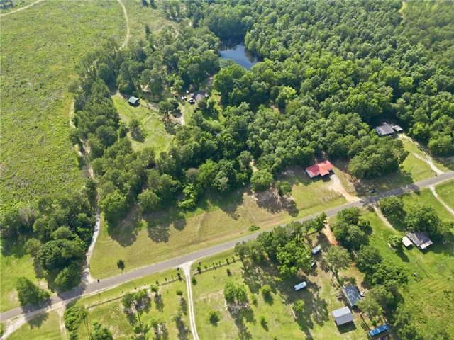 An aerial perspective reveals sprawling green landscapes and several homes nestled amongst mature trees, with a tranquil pond shimmering nearby.
