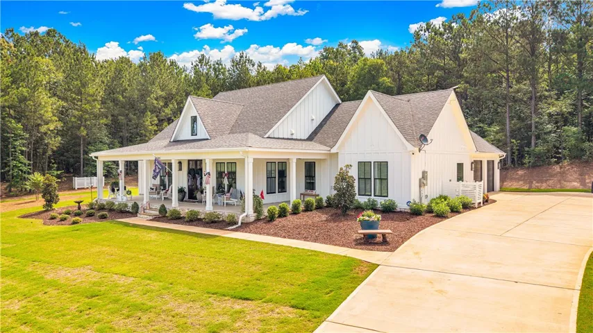 A classic farmhouse-style home with a welcoming front porch, set against a backdrop of mature trees.
