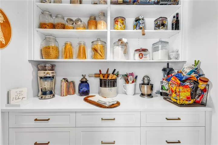 Well-organized pantry storage features open shelving and clean white cabinetry with brass hardware.