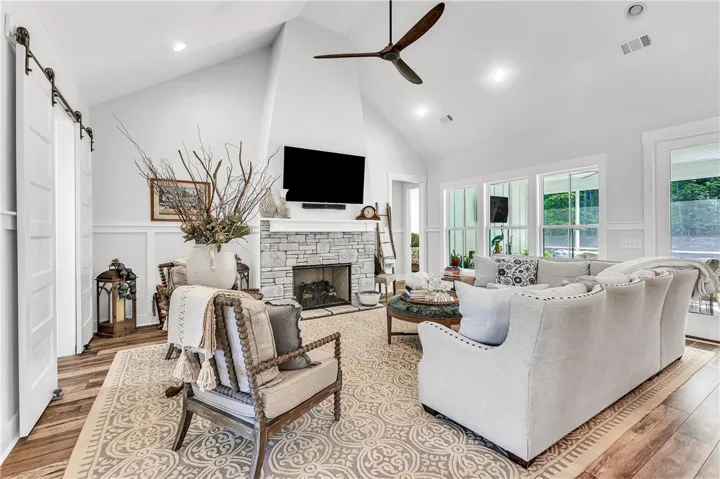 A vaulted ceiling living room features a stone fireplace, wood-look flooring, and a large area rug.