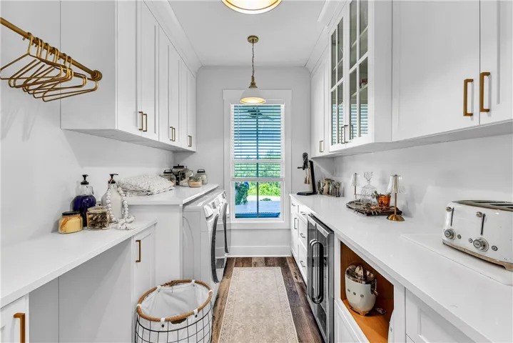 Bright laundry room featuring ample white cabinetry, sleek countertops, and a window for natural light.