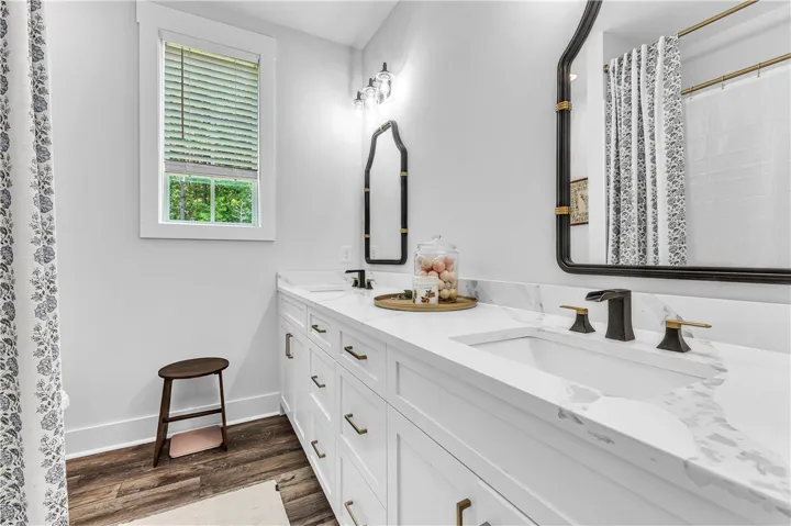 A well-lit primary bathroom features a double vanity with stone counters and rich wood flooring.