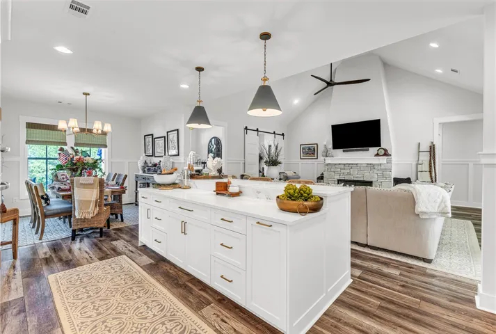 An open concept living area boasts a modern kitchen island, dining space, and a living room with a striking stone fireplace.