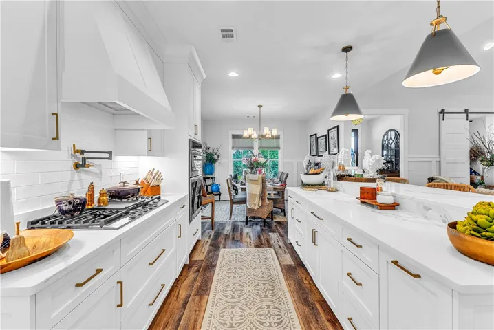 An open concept kitchen features abundant white cabinetry, a spacious island, and rich hardwood flooring, seamlessly connecting to the dining area.