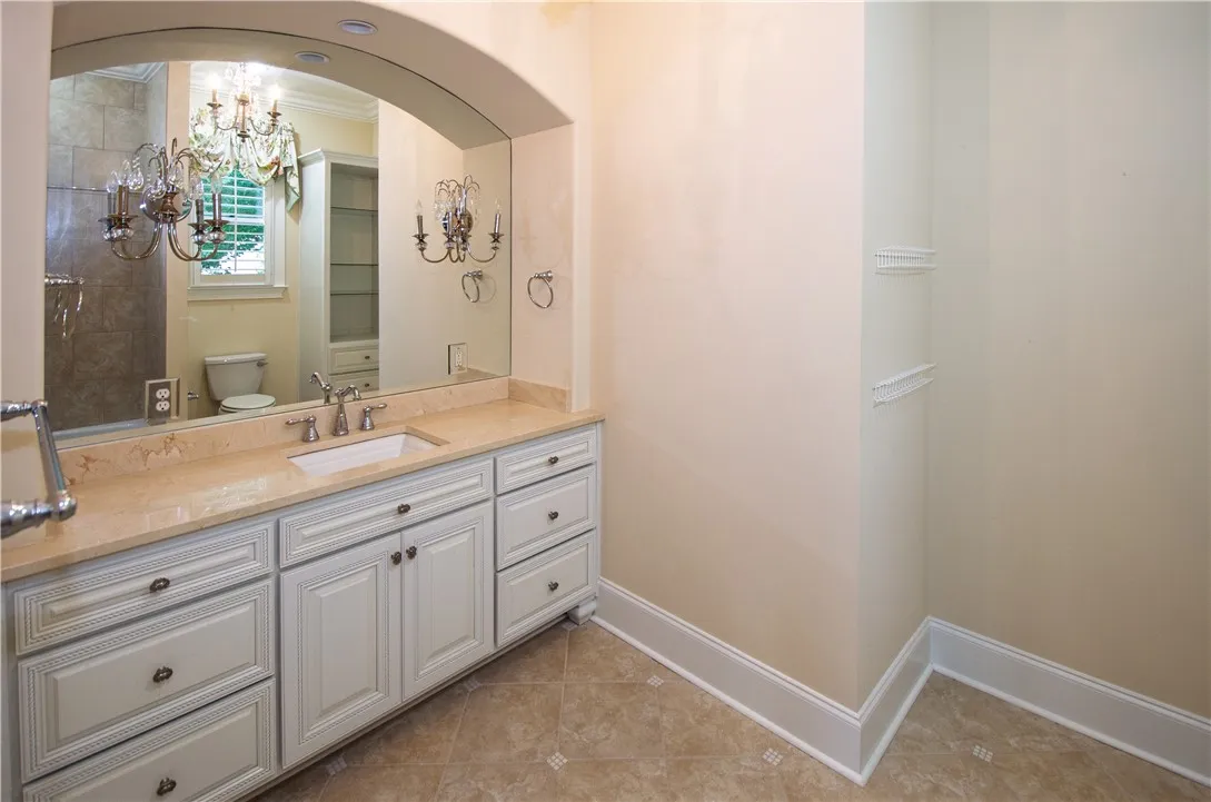 A refined bathroom featuring an elegant marble-topped vanity with a large, arched mirror and polished fixtures.