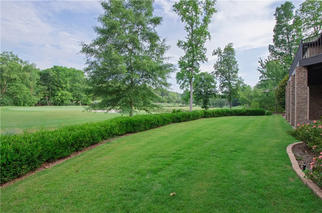 A verdant lawn gracefully transitions to a golf course, bordered by manicured hedges and mature trees.