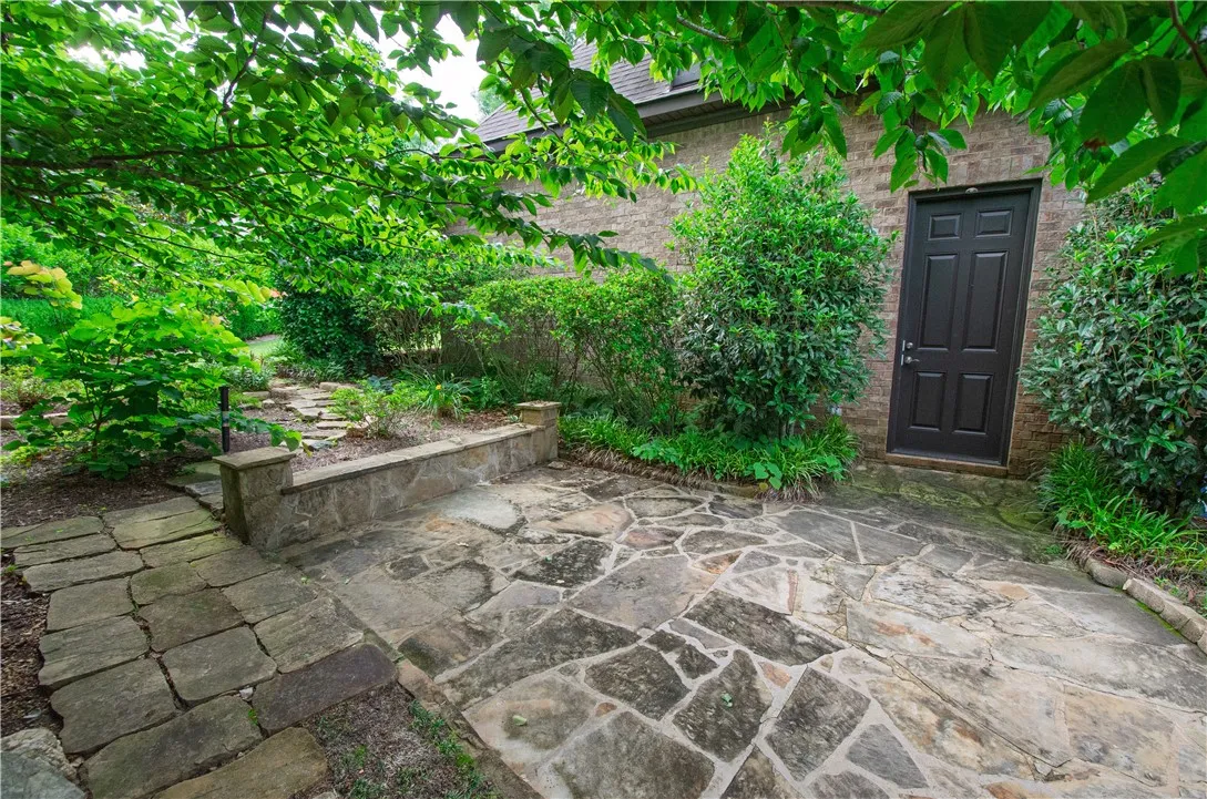 A secluded stone patio offers a private outdoor retreat, framed by lush green foliage and mature trees.