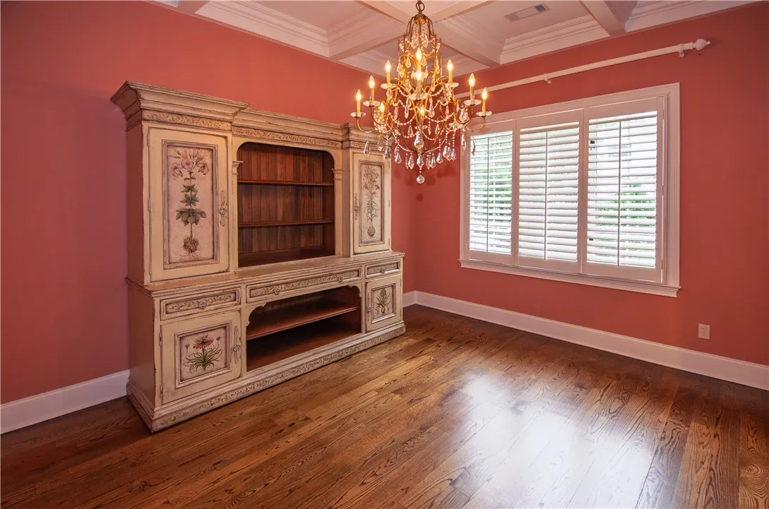 Rich hardwood floors complement an ornate chandelier and plantation-shutter windows in this versatile room.