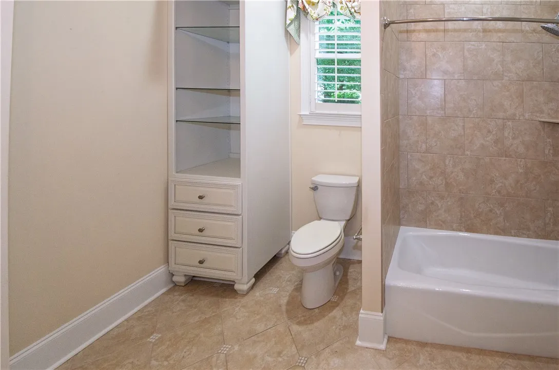 Functional bathroom featuring a tub with tiled walls and an adjacent water closet, illuminated by natural light.