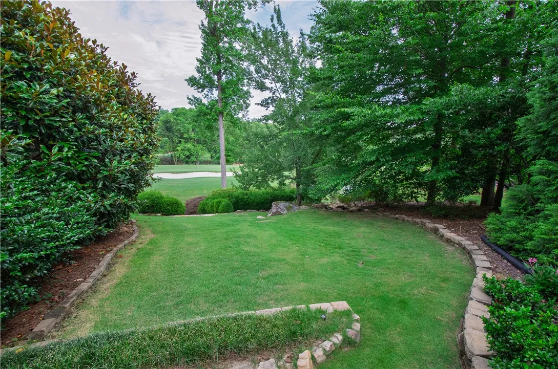A verdant lawn gracefully leads to a distant golf course, framed by established trees and natural landscaping.