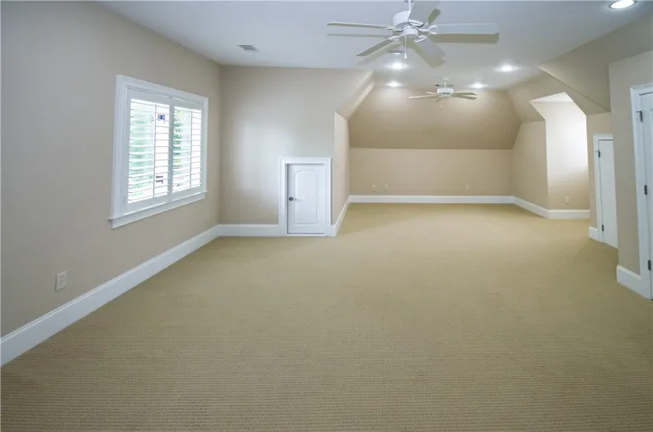 A spacious bonus room features soft carpet, bright recessed lighting, and multiple ceiling fans for comfort.