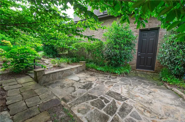A secluded stone patio offers a private outdoor retreat, framed by lush green foliage and mature trees.