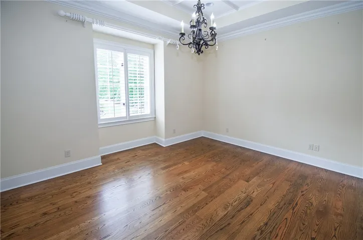 Warm hardwood flooring grounds this versatile room, crowned by an elegant chandelier and intricate ceiling details.