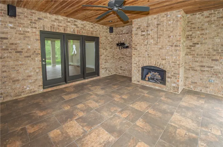 An inviting covered patio features a wood ceiling, brick fireplace, and durable tile flooring for year-round enjoyment.
