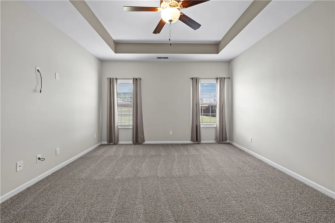 A spacious primary bedroom featuring a tray ceiling and plush carpeting.