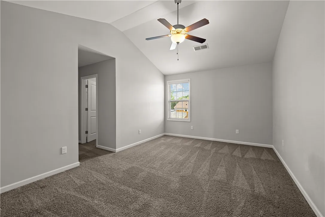 A well-lit bedroom with vaulted ceilings, featuring soft carpeting and a window offering outdoor views.