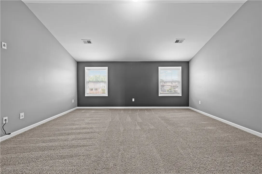 A spacious room offers comfortable carpet flooring and multiple windows, creating a versatile living space.