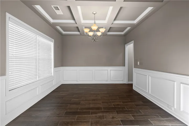 A distinguished dining room features rich wood flooring and classic wainscoting under a coffered ceiling with an elegant chandelier.