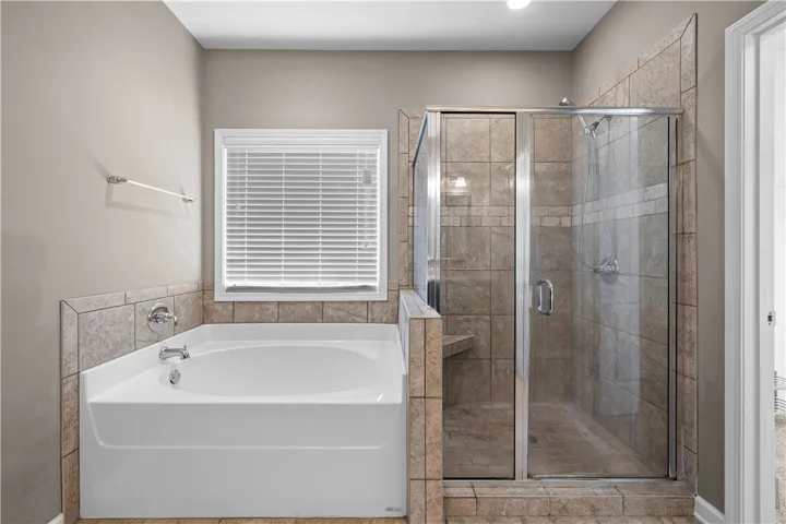Relax in this tranquil primary bathroom, offering a corner tub and a spacious, tiled walk-in shower.