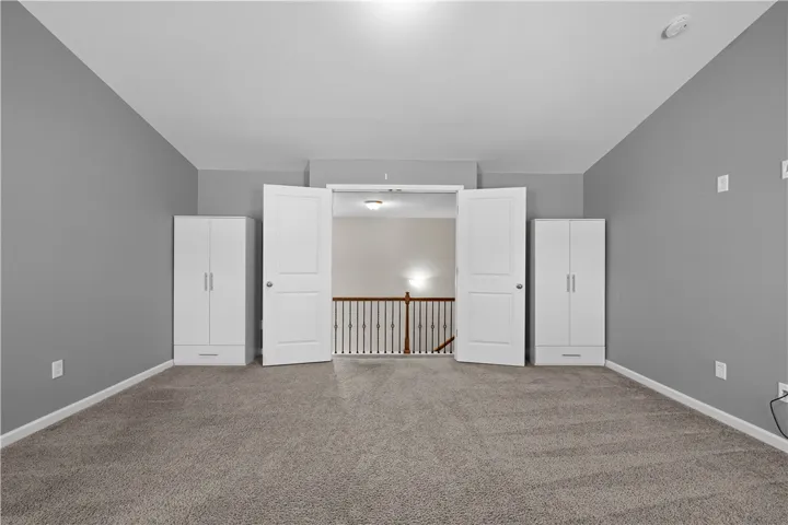 A well-lit upper level space with carpeted flooring opens to a view of the staircase below.