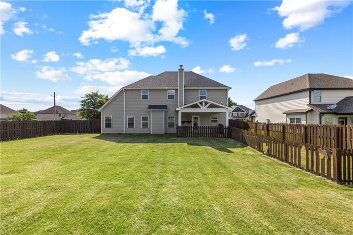 A spacious, enclosed green yard extends behind a two-story residence with a covered patio.